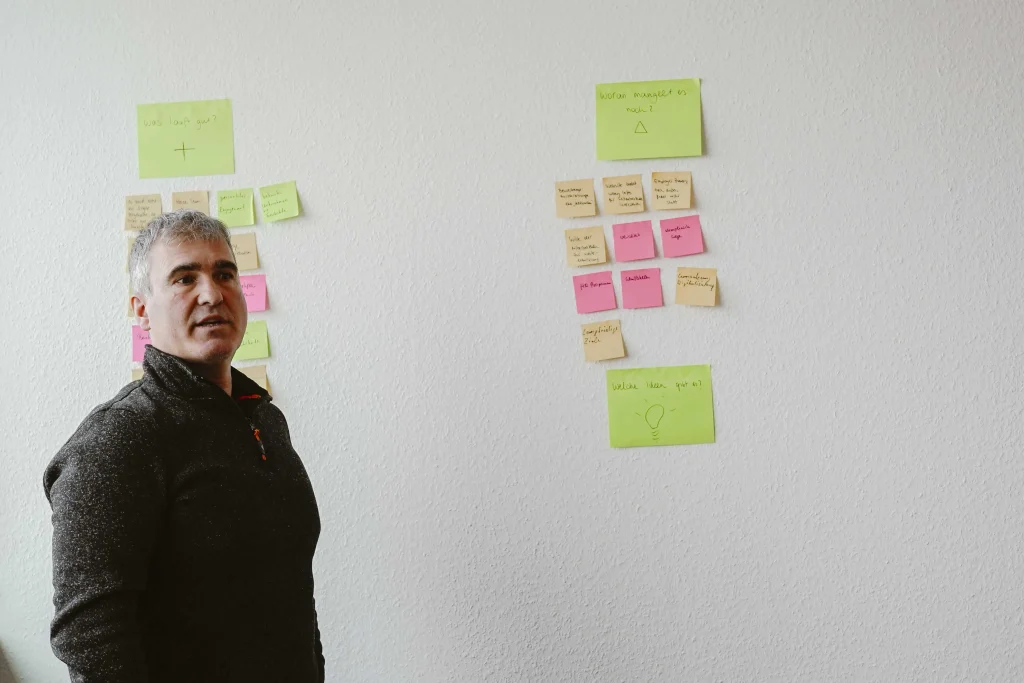 Ein Mitarbeiter spricht vor der bunten Post-It Wand über seine Vorschläge